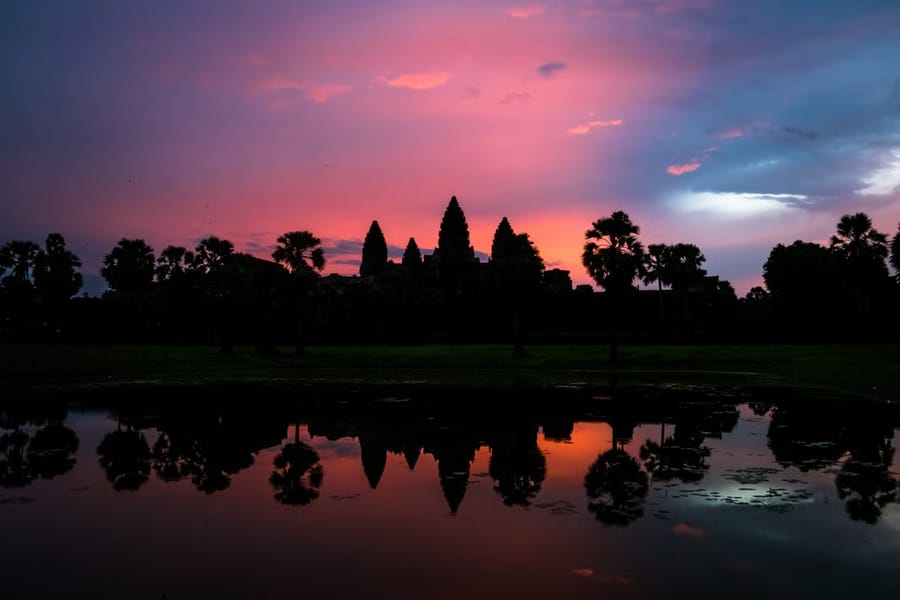 The silhouette of Angkor Wat’s five towers against a pink sunrise sky, mirrored in the temple’s reflecting pond.